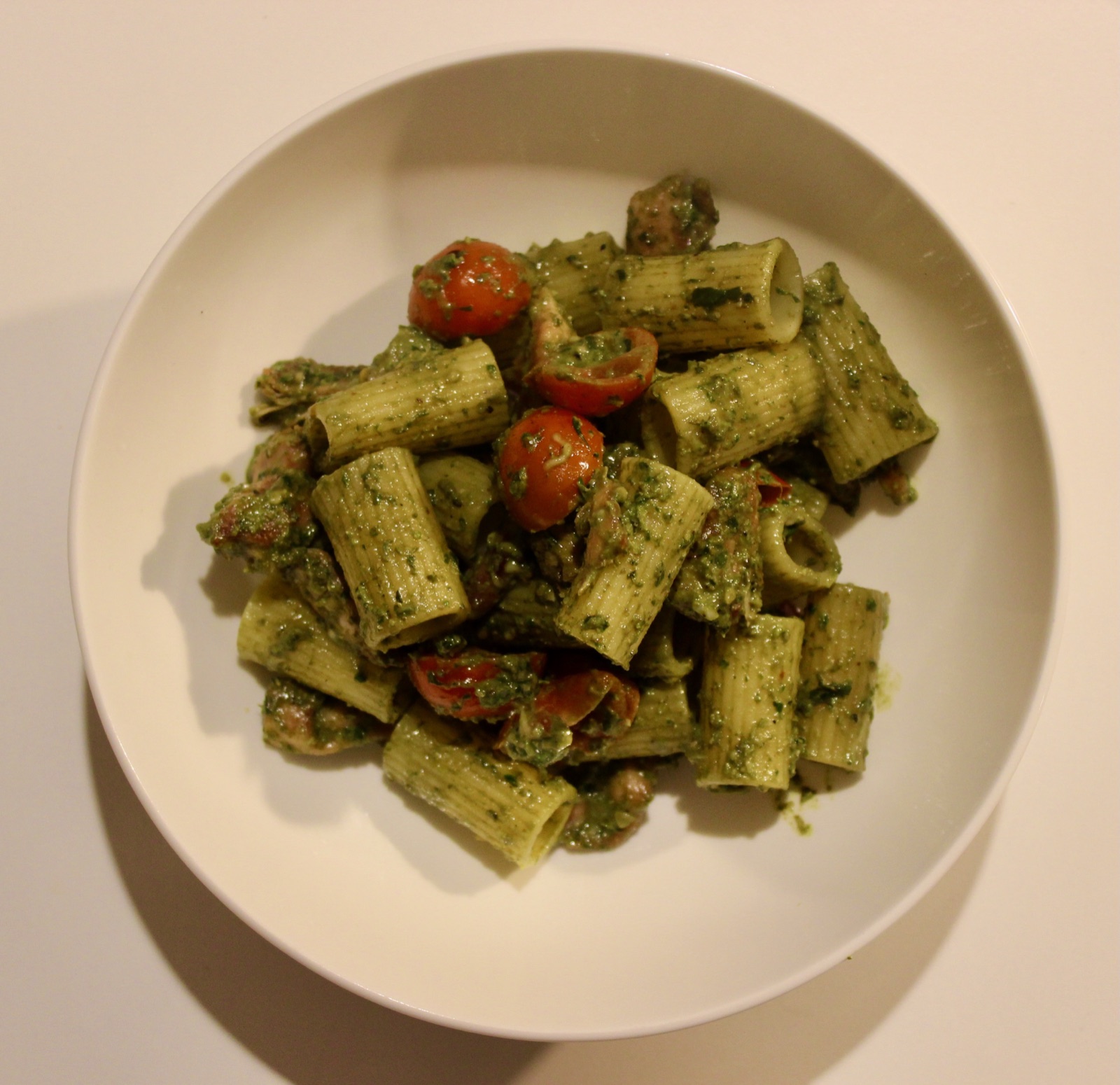 Rigatoni with basil pesto, chicken and cherry tomatoes in a white bowl