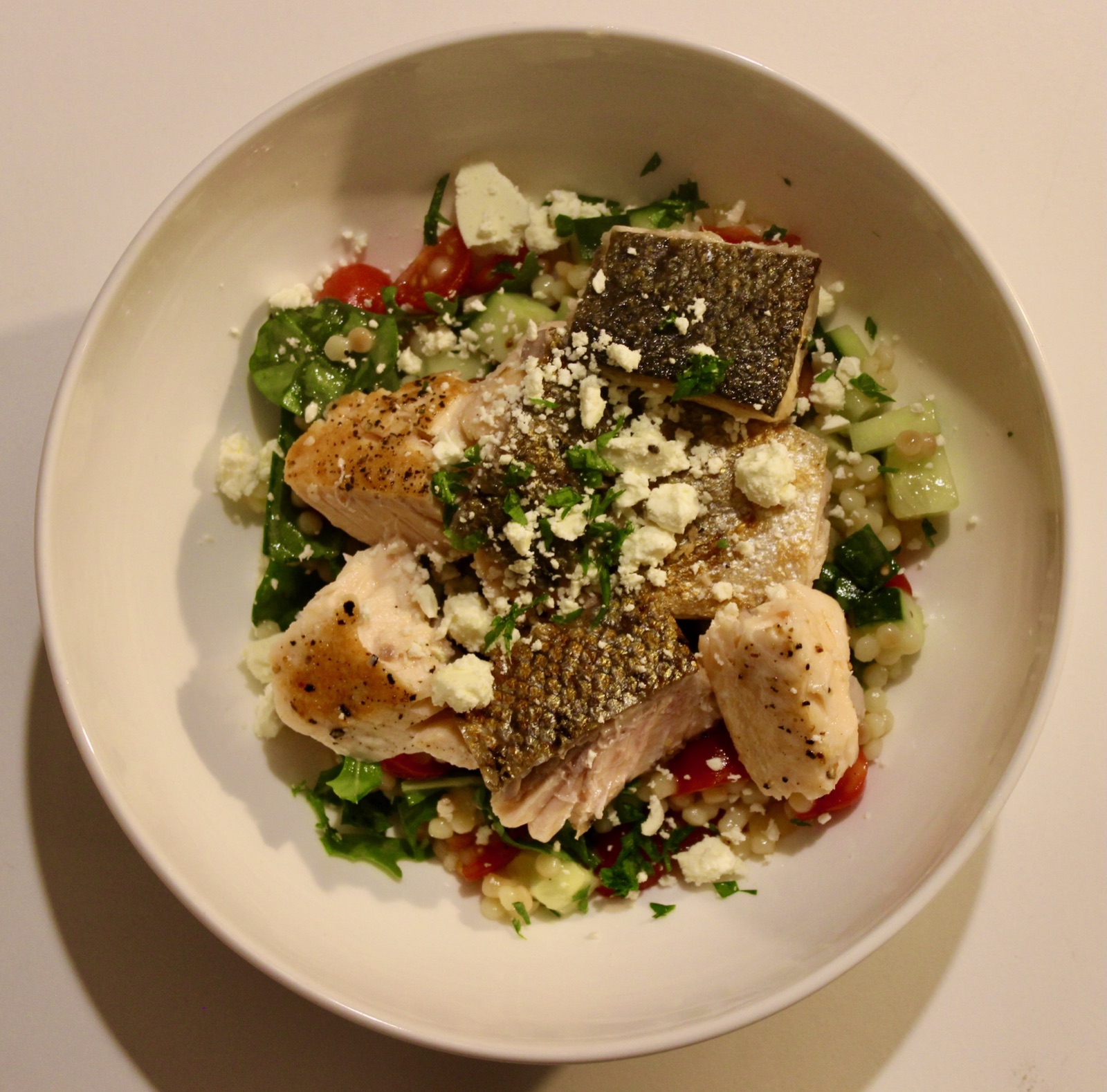 Seared salmon on pearl couscous salad with tomatoes, cucumber, greens, feta and parsley